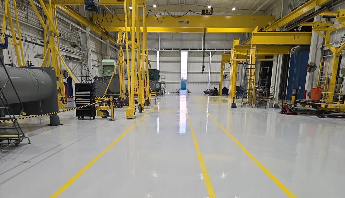 A large industrial service bay with a glossy sealed floor and yellow safety striping