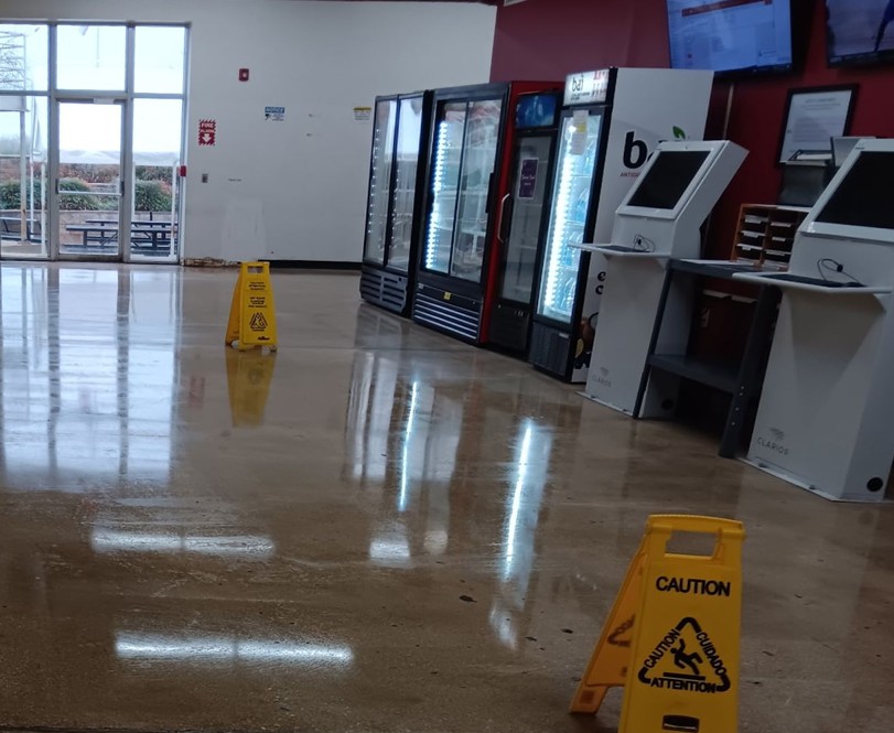 A grab and go market area with coolers and self checkout, floor freshly cleaned and signed
