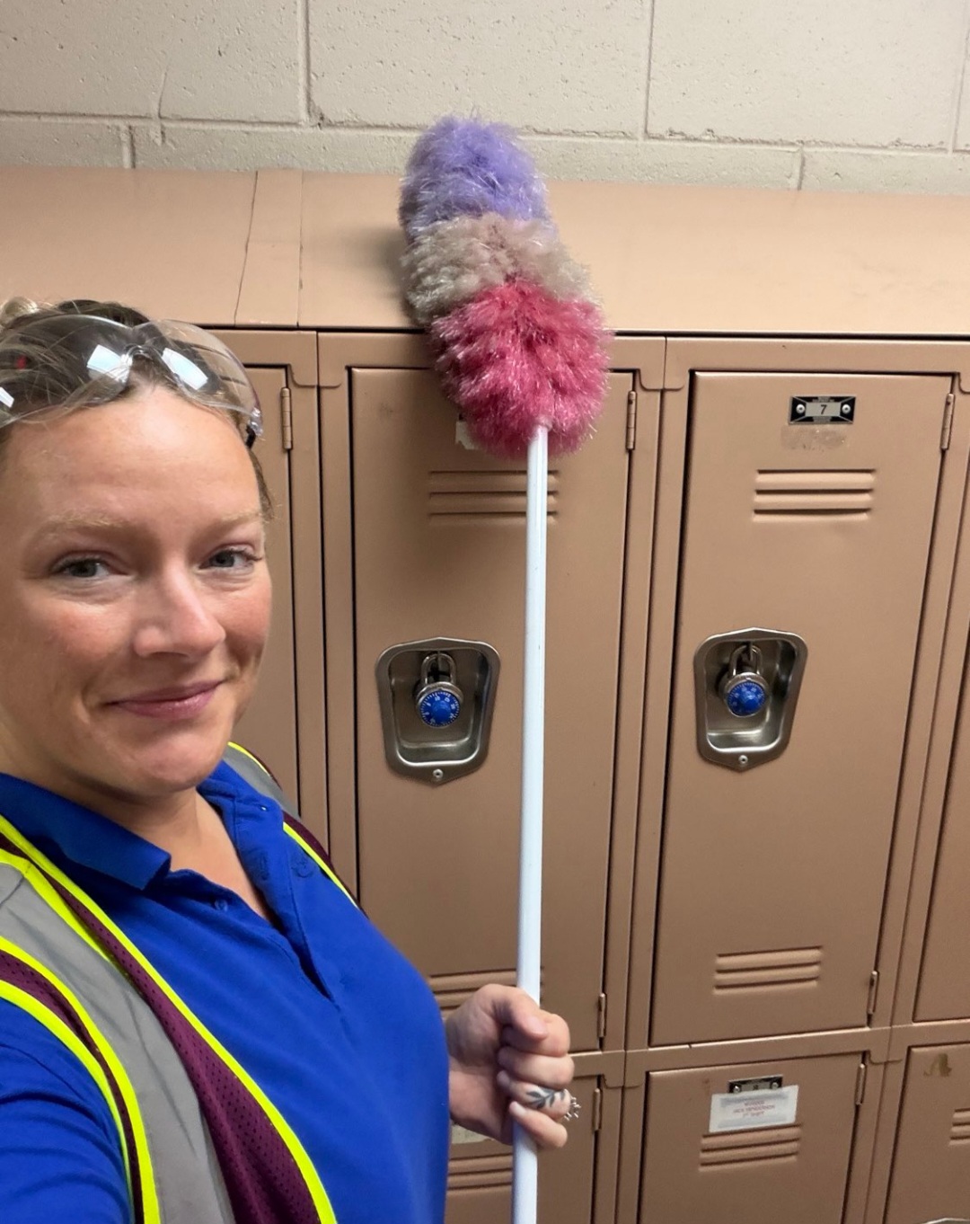 An HM Solutions crew member with a duster beside a bank of locker rooms at a campus account