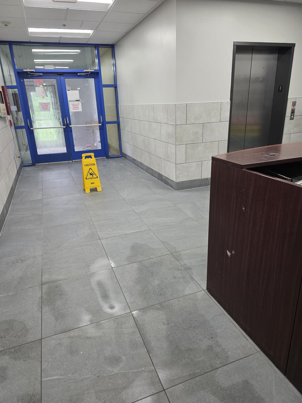 A building lobby and elevator landing at an HM Solutions account, freshly cleaned with a caution wet floor sign in place